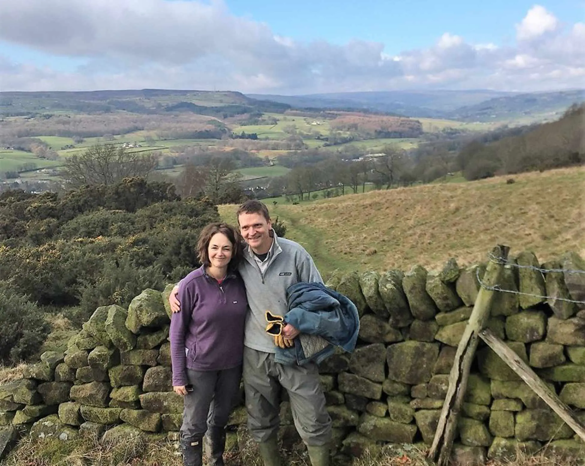 Two people standing in front of a dry stone wall and a field view